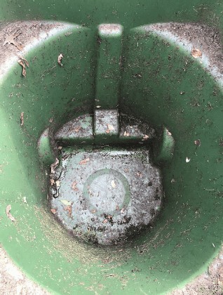 A top-down view of an empty green trash bin, its worn plastic stained with dirt and scattered dried leaves—signs that it could benefit from a professional trash can cleaning service. The inner surface shows evidence of frequent use.